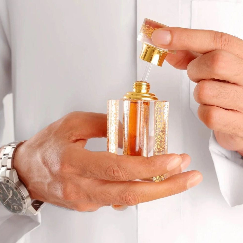 Close-up of hands holding a small perfume bottle with gold cap against a white background